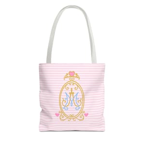 Può includere: Borsa tote a righe rosa e bianche con manico bianco. La borsa presenta un design ovale color oro con la lettera "M" blu e oro all'interno, sormontata da una corona e due cuori rosa.