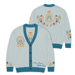 Könnte beinhalten: Hellblauer Cardigan mit türkisfarbenen Besätzen und Stickereien. Er hat eine Knopfleiste und den Text "Ave Maria, Gratia Plena". Das Design umfasst Blumen- und Herzmotive mit einem "M"-Emblem.