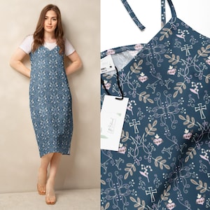 Puede incluir: Vestido azul con estampado floral blanco, usado sobre una camiseta blanca. El vestido tiene tirantes finos y un dobladillo a la rodilla. Un primer plano muestra el intrincado diseño y una etiqueta.