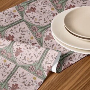 May include: A pink and green table runner with a repeating pattern of crosses, stars, and other symbols. The runner is on a wooden table with two white plates.