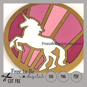 May include: A white unicorn silhouette against a pink and gold background. The unicorn is in a running pose with its head turned to the side. The background is a circle with pink and gold stripes. The text "Free2BeDigital.etsy.com" is at the bottom of the image.