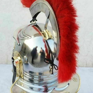 May include: A silver Roman helmet with a red horsehair plume, displayed on a wooden stand.