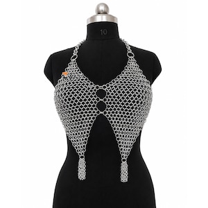 May include: A silver-toned chainmail halter top constructed from interlocking metal rings. The garment features a V-shaped front design with three central connecting rings and two dangling chain tassels at the bottom points. The text ZAFS is visible.