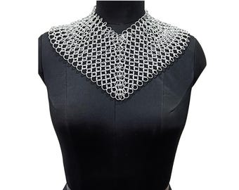 May include: A silver-toned chainmail collar necklace constructed from interlocking metal rings. The piece features a V-shaped design that drapes across the upper chest and neck area, creating a textured, metallic pattern of connected circular links.