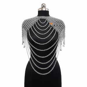 May include: A silver-toned chainmail shoulder piece featuring a high neckline and multiple cascading draped chain layers that extend across the chest. The metallic accessory is constructed from interconnected circular links and includes the text ZAFS.