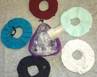 May include: Five fabric face mask covers in different colors: teal, maroon, white, black, and light blue. The covers have a hole in the center for a nose and mouth.