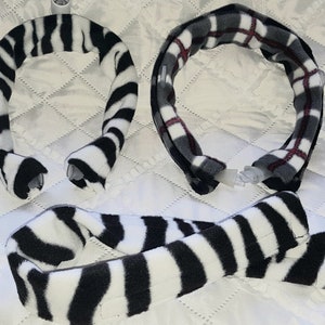 May include: Three neck wraps are displayed. Two are in a U-shape, and one is straight. One wrap has a black and white zebra stripe pattern. The other two have a plaid pattern in shades of gray and red. All have clear plastic closures.