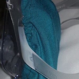 May include: A teal blue fabric earmuff with a clear plastic headband. The headband has the text "F10" printed on it.