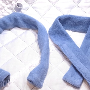 Puede incluir: Dos calientacuellos de franela azul, uno con un conector de plástico blanco en el extremo.