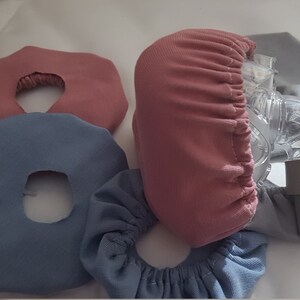 May include: Four fabric covers for a CPAP mask. Two are light blue, one is a darker blue, and one is pink.