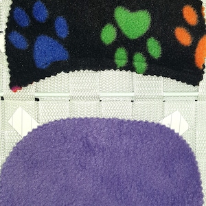 May include: Two pieces of fabric, one black with colourful paw prints and one solid purple. Both pieces are cut in a crescent shape.