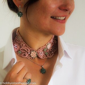 K&ouml;nnte beinhalten: Ein rosa H&auml;kelkragen mit gr&uuml;nen und wei&szlig;en Akzenten. Der Kragen wird &uuml;ber einem wei&szlig;en Hemd getragen und mit einer silbernen Kettenkette mit einem gr&uuml;nen Anh&auml;nger und Ohrringen kombiniert.