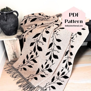 May include: A beige crochet blanket featuring a repeating black leaf and vine pattern with fringe along the edges. A pink hexagonal graphic overlay displays the text PDF Pattern and the website address hobbyistontheroad.com.