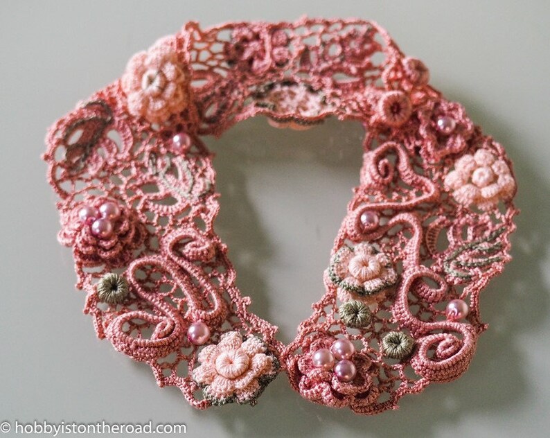 K&ouml;nnte beinhalten: Ein zartes rosa H&auml;kelkragen mit Blumenschmuck und Perlen.