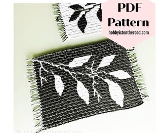 May include: Two black and white crochet coasters with a leaf design. The coasters have a fringe border. The text "PDF Pattern hobbyistontheroad.com" is on a pink hexagon.