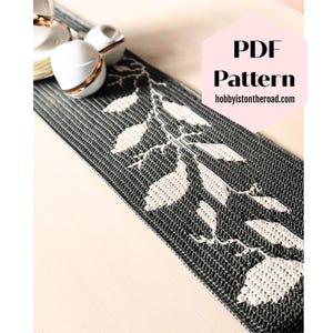 Può includere: Runner da tavolo lavorato a maglia in bianco e nero con un motivo a foglie. Il runner è rettangolare e presenta un motivo ripetuto di foglie. Il testo "PDF Pattern" e "hobbyisontheroad.com" sono visibili nell'immagine.