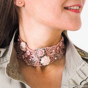 K&ouml;nnte beinhalten: Eine rosafarbene geh&auml;kelte Choker-Halskette mit floralen Verzierungen und Perlenakzenten.