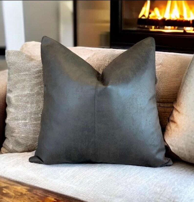 Peut inclure: Un coussin de canap&eacute; en similicuir gris fonc&eacute; avec un l&eacute;ger brillant. Le coussin est sur un canap&eacute; gris clair avec d'autres coussins.