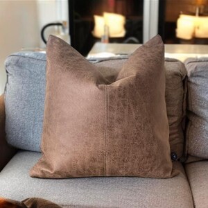 Peut inclure: Un oreiller en cuir brun avec une surface textur&eacute;e subtile. L'oreiller est rectangulaire et pr&eacute;sente une couture au centre.