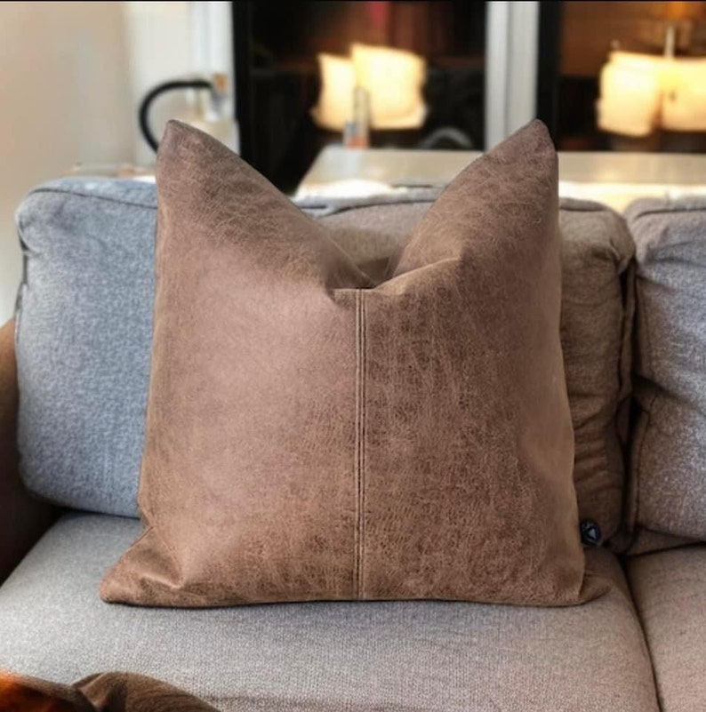 Peut inclure: Un oreiller en cuir brun avec une surface textur&eacute;e subtile. L'oreiller est rectangulaire et pr&eacute;sente une couture au centre.