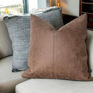 Peut inclure: Deux coussins sur un canap&eacute;. Un coussin est brun avec une surface textur&eacute;e. L'autre coussin est gris avec un motif tiss&eacute;.