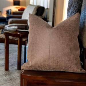 Peut inclure: Un coussin en cuir brun avec un aspect vieilli subtil. Le coussin est pos&eacute; sur une surface en bois.