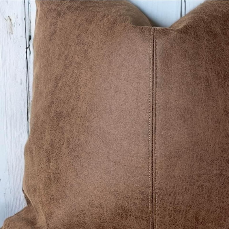 Peut inclure: Un oreiller en daim brun avec une couture au centre.