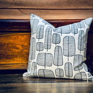 May include: A white throw pillow with a black and white geometric pattern of stylized trees. The pillow is sitting on a wooden surface.