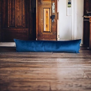 May include: A long, blue velvet bolster pillow is lying on a wooden floor in front of a closed wooden door.