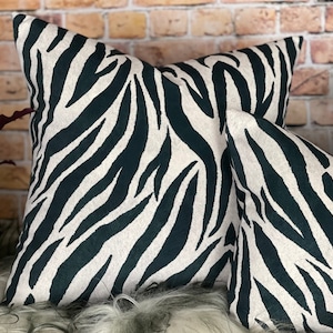 May include: Two black and white zebra print cushion covers. The cushions are made from a soft, plush fabric with a subtle sheen.