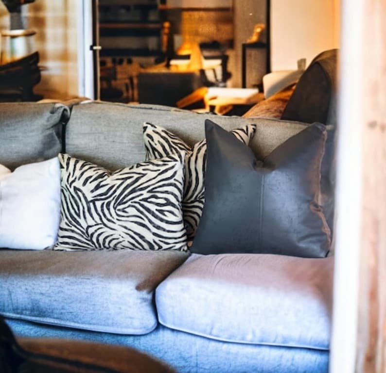 Peut inclure: Un canap&eacute; bleu clair avec trois coussins. Les coussins sont &agrave; imprim&eacute; z&egrave;bre noir et blanc, un coussin noir uni et un coussin blanc. Le canap&eacute; est dans un salon.