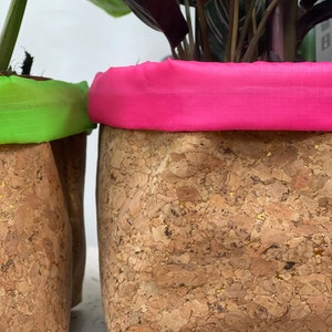 May include: Two cork planters with pink and green fabric liners. The planters are made of natural cork with a speckled pattern and gold flecks.