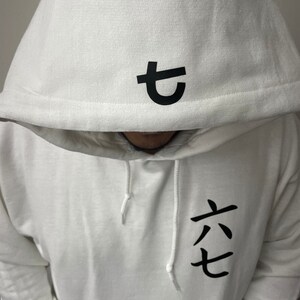 May include: White hooded sweatshirt with black Japanese characters on the hood and chest. The hood features a single character, while the chest displays three characters. The sweatshirt has white drawstrings.