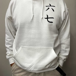 May include: White hooded sweatshirt with a front pocket and drawstring. The sweatshirt features black Japanese characters on the upper left chest. The person is wearing khaki pants and a black belt.