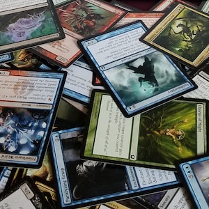 May include: A large pile of colorful trading cards featuring fantasy creatures and illustrations. The cards are arranged in a random order, with some cards overlapping others.