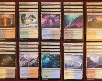 May include: A collection of Magic: The Gathering land cards, featuring various landscapes like caves, forests, and mountains. Each card has unique artwork and text, with names such as "Bloodfell Caves" and "Rugged Highlands". The cards are arranged in neat rows.