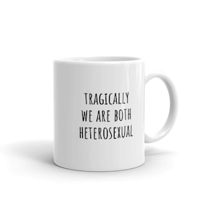 May include: White ceramic coffee mug with black text that reads "Tragically We Are Both Heterosexual".