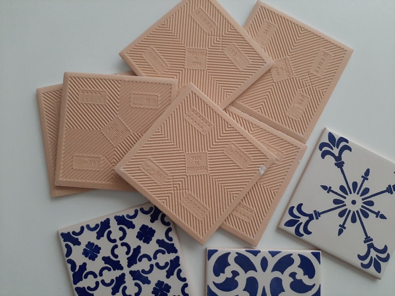 May include: A set of six beige ceramic tiles with a textured surface and the words "Made in Portugal" printed on them. There are also two white ceramic tiles with blue floral patterns.