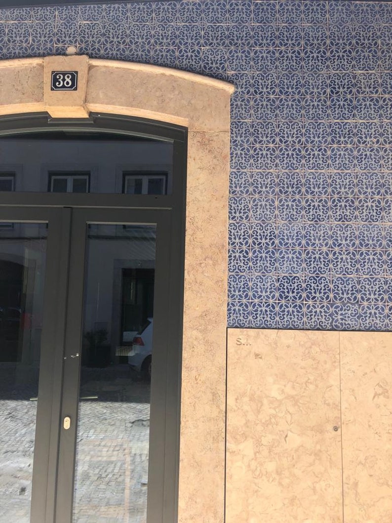 May include: A building with a black door and a tiled facade. The tiles are blue and white with a floral pattern. The door has a number "38" above it.