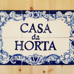 Pode incluir: Um sinal de azulejo de cerâmica branca com desenhos florais azuis e o texto "CASA da HORTA" em letras azuis.