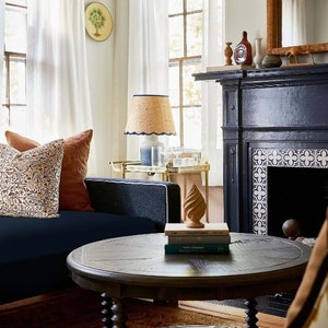 May include: A dark wood coffee table with a round top and twisted legs. The table is in a living room with a blue sofa, a fireplace, and a rug.