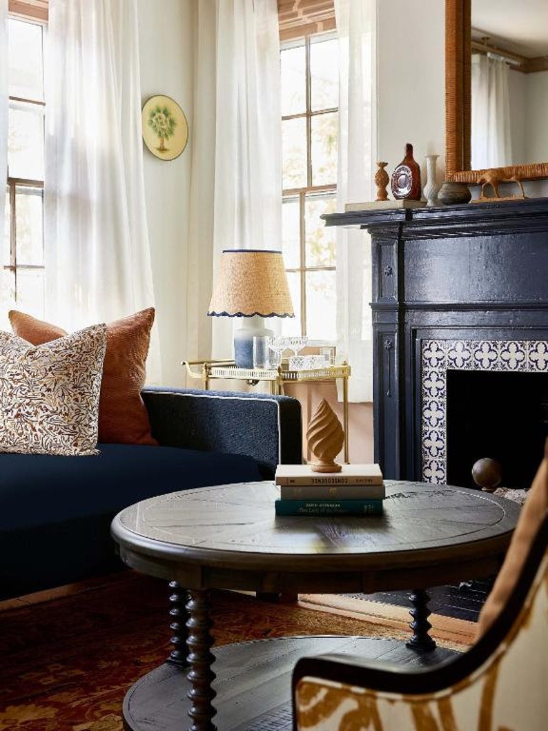May include: A dark wood coffee table with a round top and twisted legs. The table is in a living room with a blue sofa, a fireplace, and a rug.