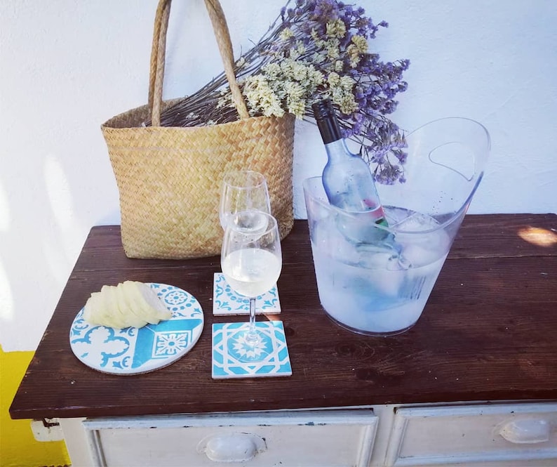 Peut inclure: Une table en bois avec un sac en osier, deux verres &agrave; vin, une bouteille de vin dans un seau &agrave; glace transparent et un dessous-de-verre en carrelage bleu et blanc.
