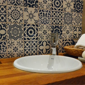 May include: A white porcelain bathroom sink with a chrome faucet, a white soap dispenser, a white soap dish, a white towel, and a wicker basket on a wooden countertop. The wall behind the sink is tiled with blue and white patterned tiles.