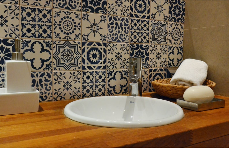 May include: A white porcelain bathroom sink with a chrome faucet, a white soap dispenser, a white soap dish, a white towel, and a wicker basket on a wooden countertop. The wall behind the sink is tiled with blue and white patterned tiles.