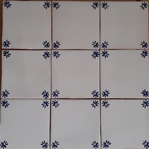 Op de afbeelding: Negen witte keramische tegels met blauwe bloemmotieven in de hoeken. De tegels zijn gerangschikt in een 3x3 raster.
