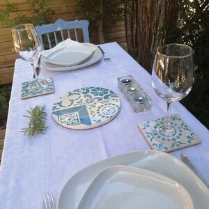 Peut inclure: Une nappe blanche avec un dessous de plat &agrave; motifs bleus et blancs, deux assiettes blanches, deux verres &agrave; vin, un brin de romarin et trois bougies chauffe-plat dans des bougeoirs en verre.
