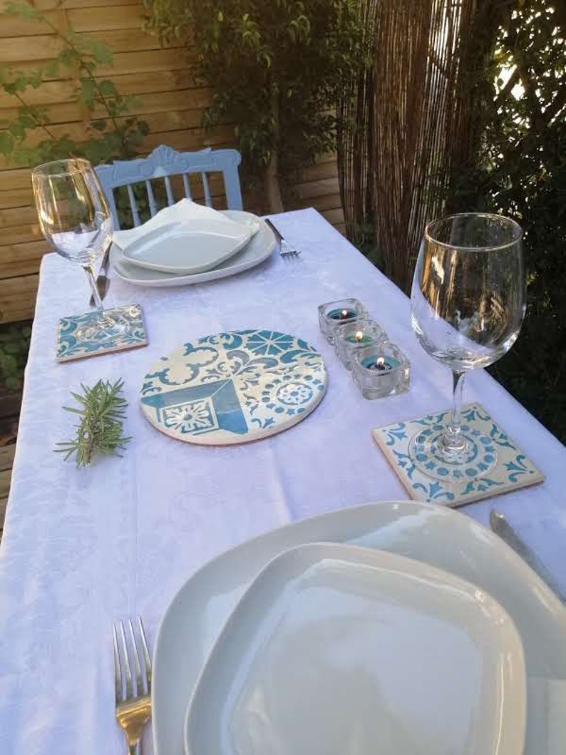 Peut inclure: Une nappe blanche avec un dessous de plat &agrave; motifs bleus et blancs, deux assiettes blanches, deux verres &agrave; vin, un brin de romarin et trois bougies chauffe-plat dans des bougeoirs en verre.