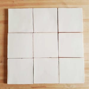 May include: Nine white ceramic tiles arranged in a 3x3 grid on a wooden surface.