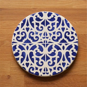 Könnte beinhalten: Ein runder Untersetzer aus Keramik mit einem komplizierten blauen und weißen Muster. Der Untersetzer zeigt ein sich wiederholendes Design aus stilisierten floralen Motiven.